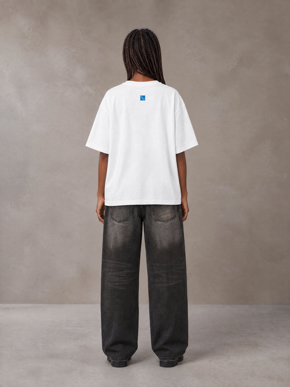Model wearing the SM Script T-shirt in Lucent White, rear view.