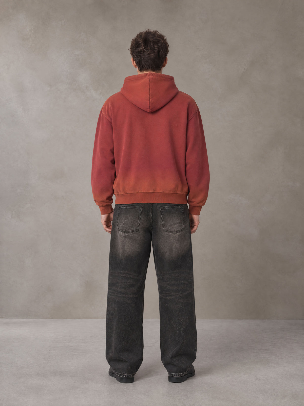 Model wearing the SM Script Washed Hoodie in Copper Rust, rear view.