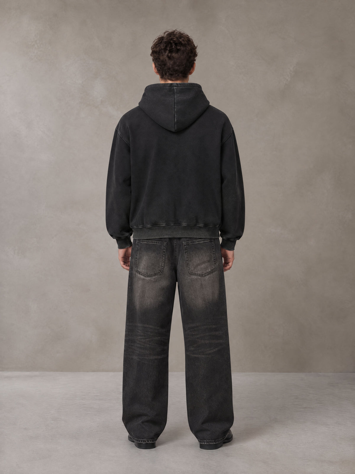 Model wearing the SM Script Washed Hoodie in Midnight Black, rear view.