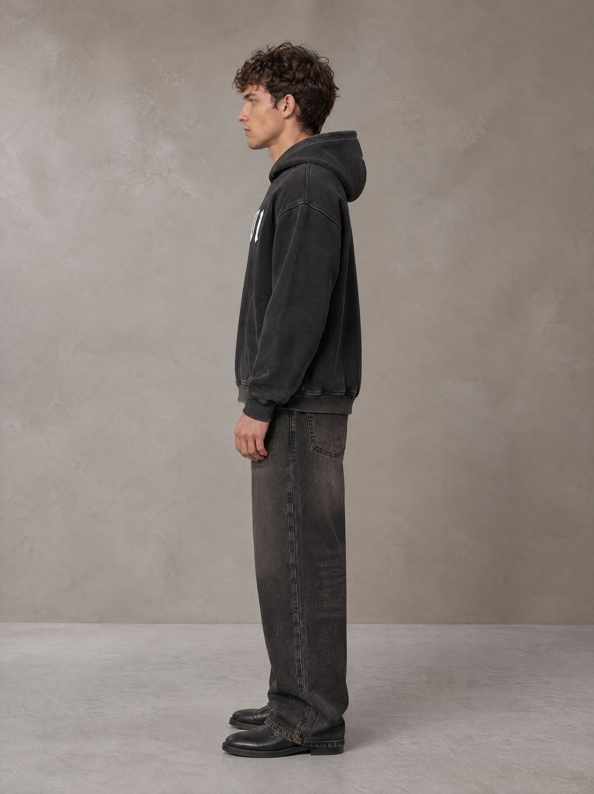 Model wearing the SM Script Washed Hoodie in Midnight Black, side profile.