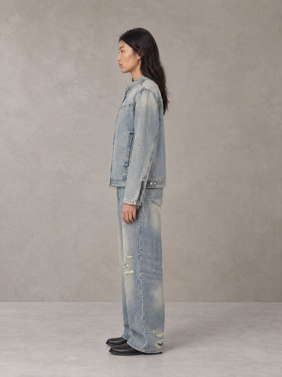 Model wearing the SM Vintage Wash Zip Denim Jacket and SM Heritage Distressed Denim Jeans in Cadet Grey, side profile.