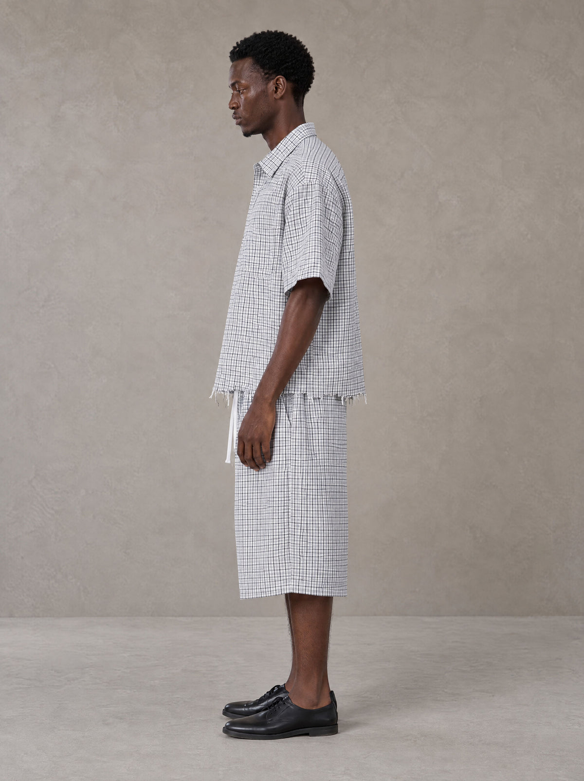 Model wearing the SM Distressed Plaid Boxy Shirt and SM Plaid Capri Shorts in Lucent White, side profile.
