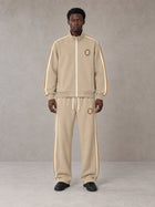 Model wearing the SM Insignia Track Jacket in Oatmeal Cookie with the SM Insignia Track Trousers in Soft Beige, front view.