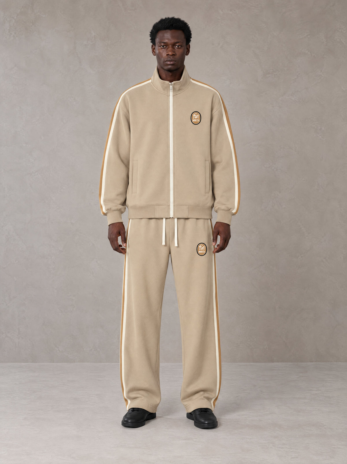 Model wearing the SM Insignia Track Jacket in Oatmeal Cookie with the SM Insignia Track Trousers in Soft Beige, front view.