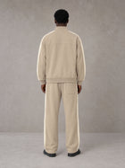Model wearing the SM Insignia Track Jacket in Oatmeal Cookie with the SM Insignia Track Trousers in Soft Beige, rear view.