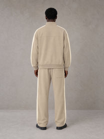 Model wearing the SM Insignia Track Jacket in Oatmeal Cookie with the SM Insignia Track Trousers in Soft Beige, rear view.