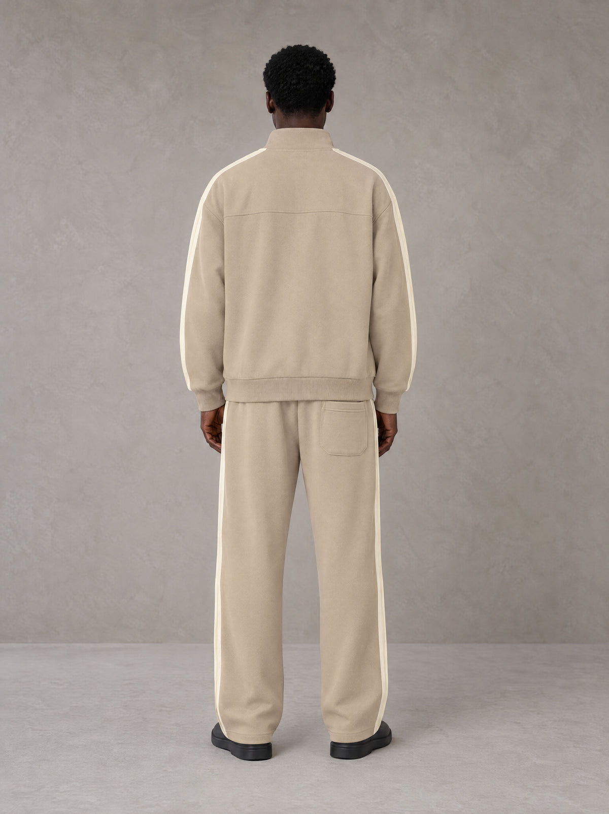 Model wearing the SM Insignia Track Jacket in Oatmeal Cookie with the SM Insignia Track Trousers in Soft Beige, rear view.