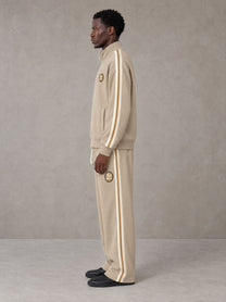 Model wearing the SM Insignia Track Jacket in Oatmeal Cookie with the SM Insignia Track Trousers in Soft Beige, side profile view.