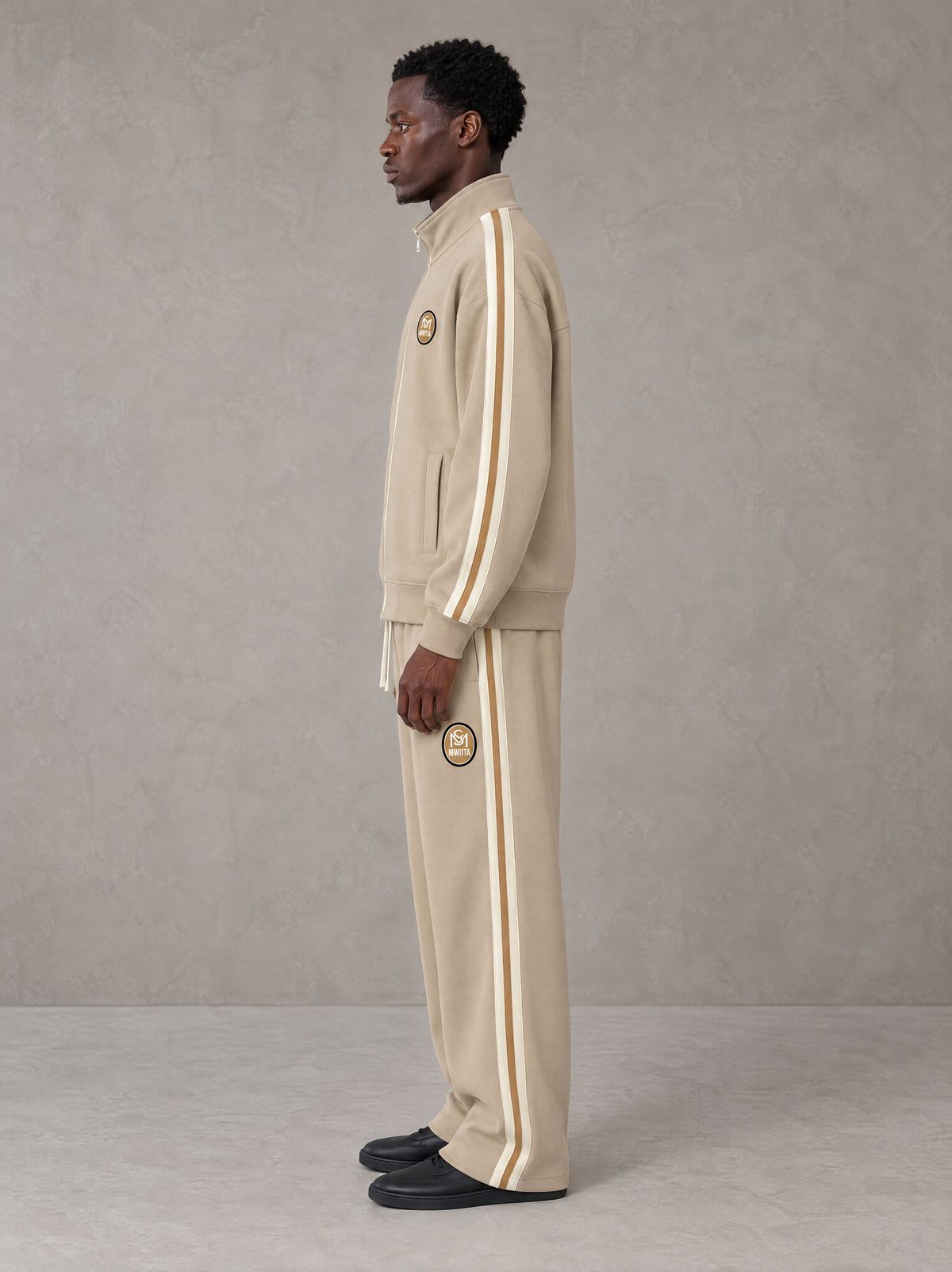 Model wearing the SM Insignia Track Jacket in Oatmeal Cookie with the SM Insignia Track Trousers in Soft Beige, side profile view.