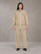 Model wearing the SM Insignia Track Jacket in Oatmeal Cookie with the SM Insignia Track Trousers in Soft Beige, front view.