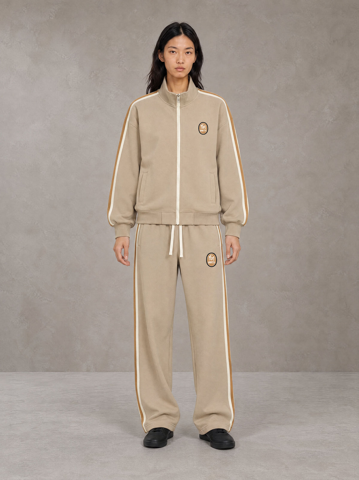 Model wearing the SM Insignia Track Jacket in Oatmeal Cookie with the SM Insignia Track Trousers in Soft Beige, front view.