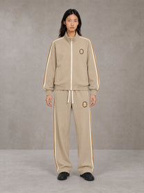 Model wearing the SM Insignia Track Jacket in Oatmeal Cookie with the SM Insignia Track Trousers in Soft Beige, front view.
