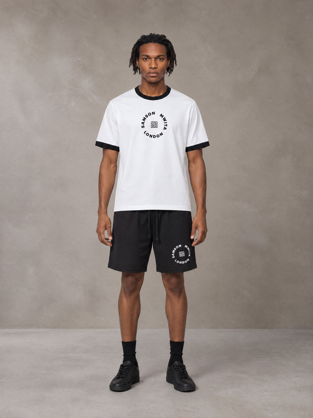 Model wearing the SM London T-shirt in Lucent White with the SM London Shorts in Midnight Black, front view.