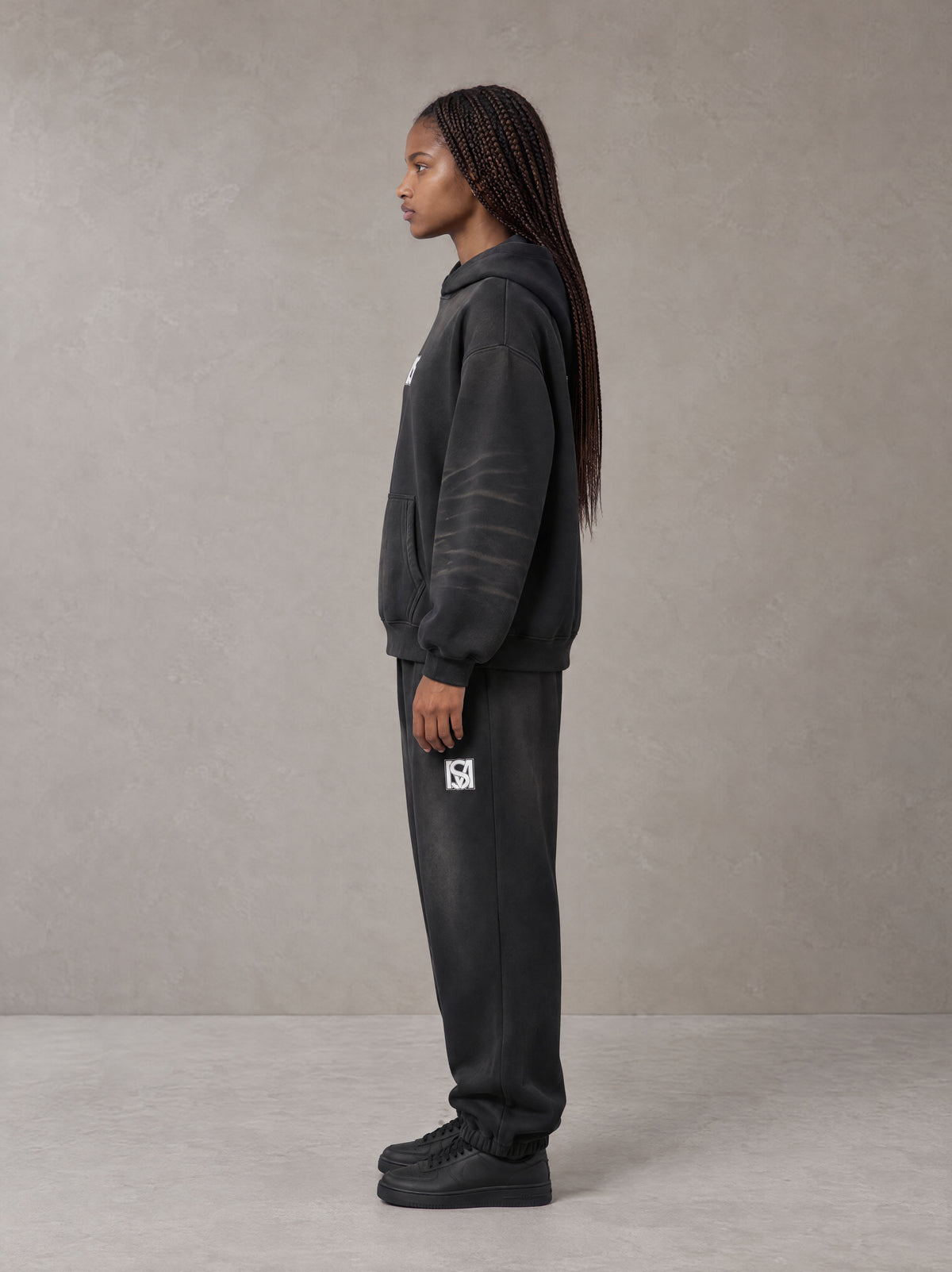 Model wearing the SM Monkey Washed Fleece Hoodie in Midnight Black with the SM Monkey Washed Jogger Sweatpants in Midnight Black, side profile view.